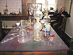 Interiör från Alfred Nobels laboratorium. Längst bort till höger ses Alfred själv sitta och fundera.